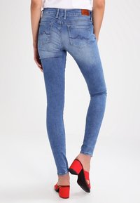 Jeans de mezclilla azul ajustados con un acabado deslavado, que presentan dos bolsillos traseros con costuras curvas, combinados con sandalias rojas de tacón.
