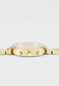 Gold-tone watch with a round face, crystal embellishments, and three knobs on the side. Metal link band complements the design.
