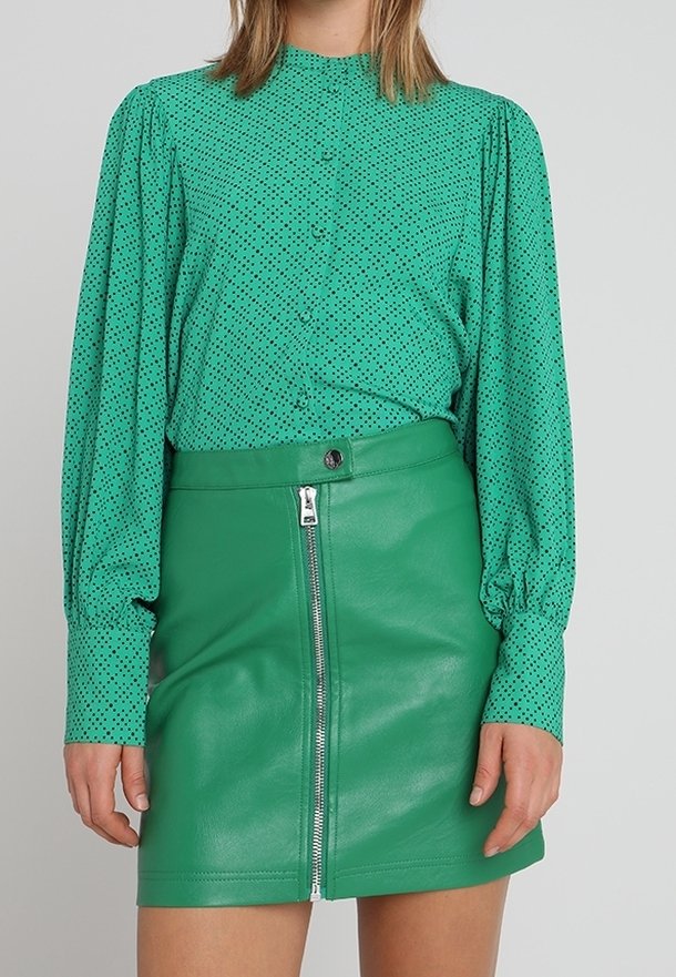 Chemisier vert à pois avec de longues manches bouffantes, boutons à l'avant, associé à une jupe mini en cuir vert dotée d'une fermeture éclair à l'avant et d'une fermeture à pression.