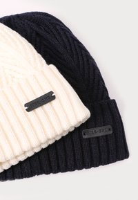 Two knitted beanies: one cream and one navy blue. Both feature ribbed texture and a black leather label with "PIER-ONE" attached.