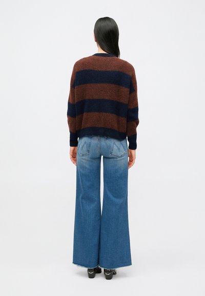 Pulover în dungi maro și bleumarin, cu croială lejeră; asortat cu blugi largi, cu talie înaltă, de culoare albastru deschis, cu aspect decolorat și tiv destrămat.