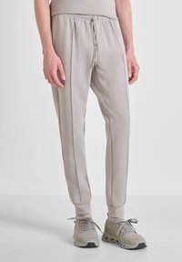 Pantalones jogger beige fabricados con material suave y elástico. Cuenta con una cintura elástica con cordón, costuras laterales y puños acanalados.