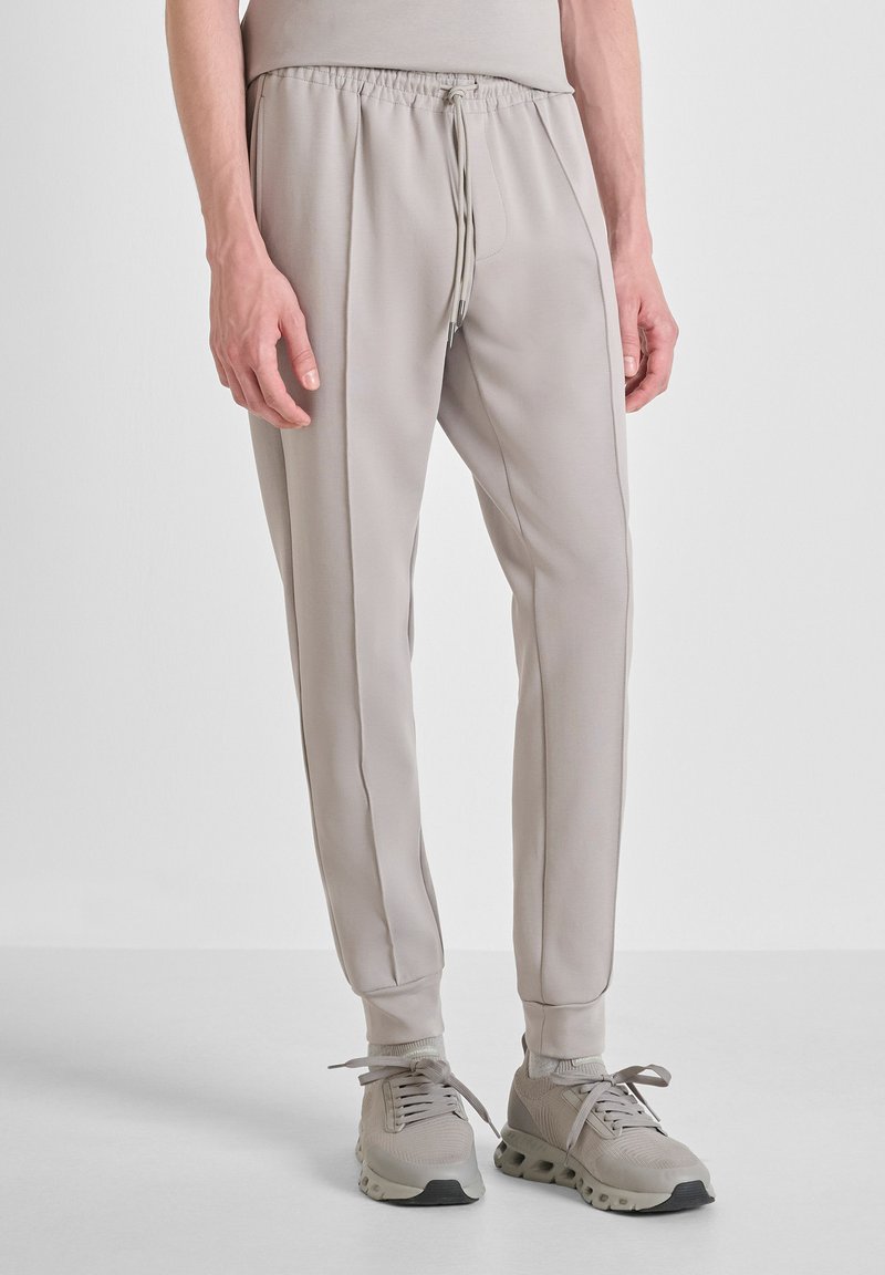 Pantalones jogger beige fabricados con material suave y elástico. Cuenta con una cintura elástica con cordón, costuras laterales y puños acanalados.