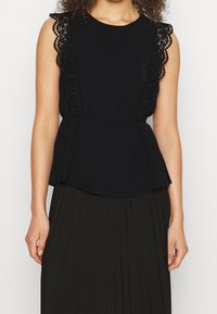 Černý peplum top s krajkovými detaily na ramenou. Hladká látka, kulatý výstřih a rozšířený lem. Nosený s plisovanou tmavou sukní.