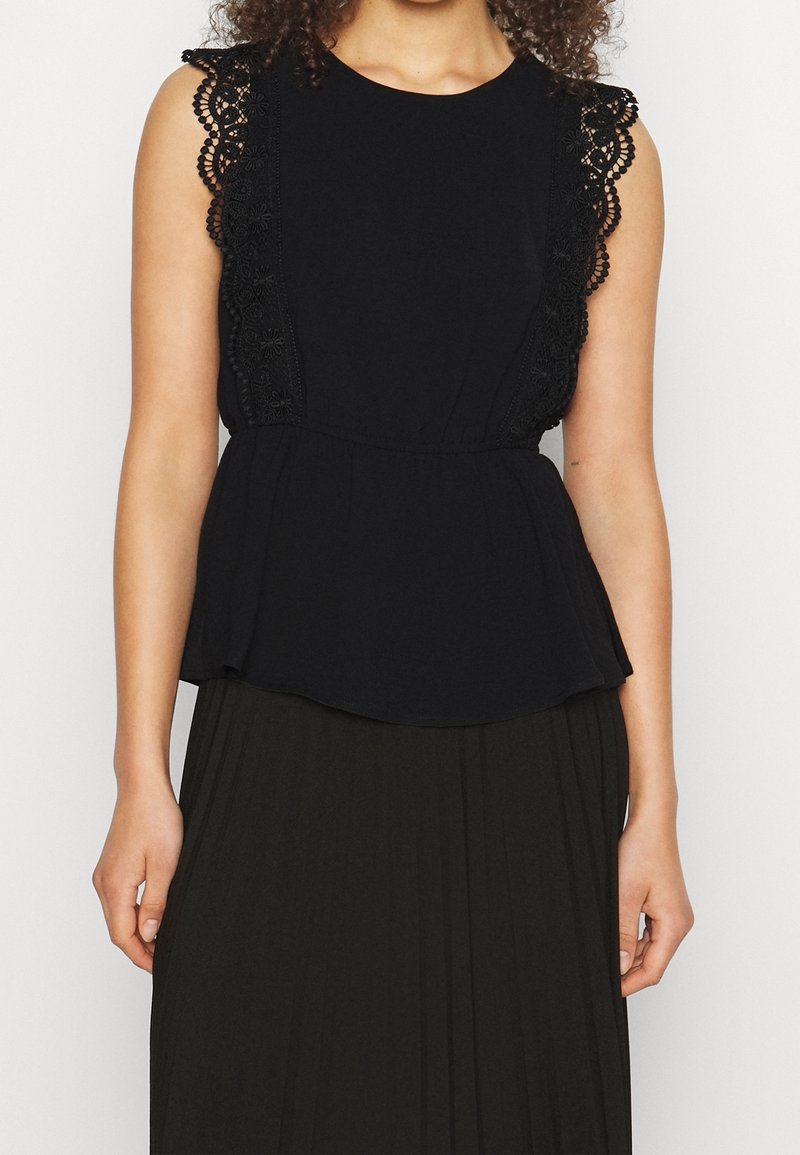 Černý peplum top s krajkovými detaily na ramenou. Hladká látka, kulatý výstřih a rozšířený lem. Nosený s plisovanou tmavou sukní.