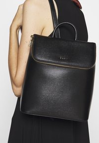 Czarny skórzany plecak o gładkiej teksturze, złoty zamek błyskawiczny i górna rączka. Charakteryzuje się minimalistycznym designem z przednią kieszenią.