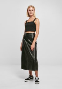 Top corto nero con scollatura quadrata, abbinato a una gonna lunga in pelle nera a vita alta con dettagli delle cuciture e spacchi laterali. Sneakers nere.