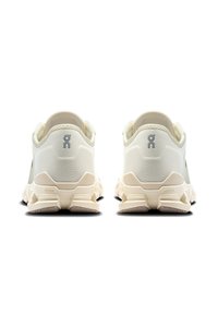 Zapatillas de color neutro con una parte superior texturizada, suela acolchada y un diseño de tacón distintivo. Presentan detalles de logotipo y una tracción robusta.