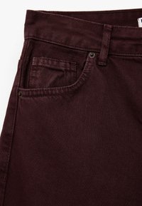 Bordeaux denim jeans met een gestructureerde afwerking, voorzien van een voorzak, metalen knoopsluiting en contrasterende stiksels langs de tailleband.