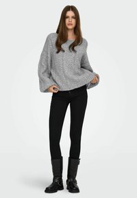 Grijze gebreide trui met een gestructureerd ontwerp, wijde mouwen, gecombineerd met zwarte skinny jeans en hoge zwarte laarzen met gespen.