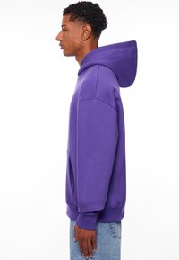 Paarse hoodie met een buidelzak, ribbels bij de mouwen en onderkant. Gemaakt van zacht materiaal met een ontspannen pasvorm, met een gladde textuur.
