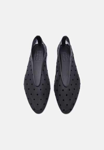 Μαύρα πλαϊνά παπούτσια με μυτερή μύτη και λεπτό ύφασμα με μικρές βελούδινες πουά, απεικονιζόμενα από επάνω σε λευκό φόντο.