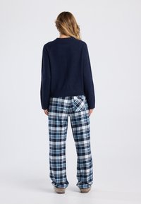 Navy knitted sweater with a round neckline paired with blue plaid flannel pants featuring a back pocket and soft texture.