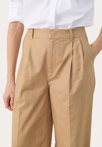 Cotton trousers in light brown with a pleated front, wide-leg cut, and side pockets. Smooth texture with a clean finish.