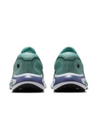 Turkusowe buty sportowe z teksturowanej tkaniny, z wyściółką w okolicach pięty oraz białą podeszwą środkową z purpurowym akcentem. Widoczna czarna gumowa podeszwa.