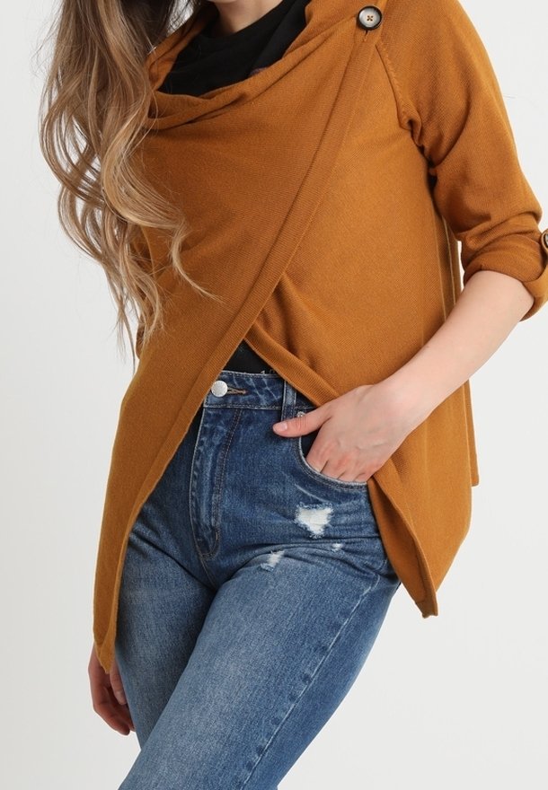 Mosterdkleurige wikkeltop met een col-halslijn en een enkele knoopdetail, gecombineerd met versleten blauwe denim jeans.