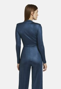 Langdurige jumpsuit van diepblauwe satijnen stof, met een getailleerde top en brede pijpen, die een gladde textuur en een stijlvolle uitstraling benadrukt.