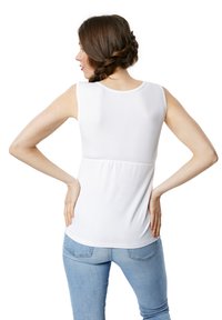 Top bianco senza maniche con scollatura tonda, elastico arricciato in vita e tessuto liscio. Indossato con jeans azzurri chiari.