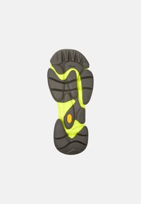 Vibram-pohja on varustettu harmaalla kumipohjalla, jossa on teksturoitu uritus ja kirkas keltainen tartuntakuviollisuus; sisältää erottuvan oranssin logon korostuksen.