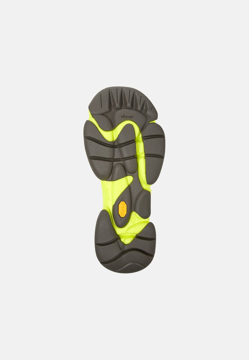 La semelle Vibram présente une base en caoutchouc gris avec des rainures texturées et un motif de grip jaune vif ; elle inclut un accent de logo orange distinct.