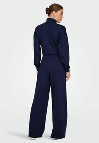 Ensemble coordonné bleu marine comprenant un col montant, une coupe décontractée et un pantalon large. Confectionné dans un tissu doux au toucher lisse.