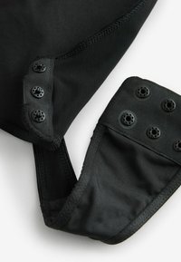 Prenda negra hecha de tejido suave y malla, con cierres a presión y un diseño estructurado, con detalles de costura a lo largo de los bordes.