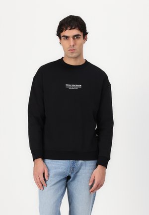 Sort sweatshirt med rund halsudskæring og ribstrikkede manchetter. Har et frontlogo i hvidt, parret med lyseblå denimjeans.