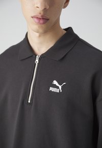 Zwarte rits polo shirt gemaakt van een katoenmix, met korte mouwen, een kraag en een wit Puma-logo op de linkerborst.