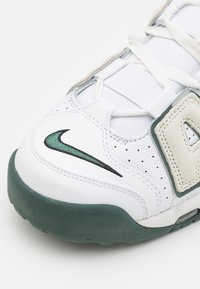 Scarpa da ginnastica bianca con suola in gomma verde, caratterizzata da un logo Nike swoosh ricamato in nero e verde, dettagli in rete e fori traforati.