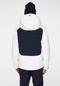 Vit jacka med en marinblå vadderad bakdel och huva, kompletterad med mörkblå accenter. Slät textur, minimalistik design.