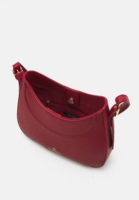 Punainen kangasolkaistuotepussi, jossa on sileä pinta, kultaiset välinetehot ja magneettinappi. Sisäpuolella on vetoketjutasku järjestämistä varten.