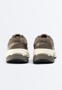 Paar brauner Netzsneaker mit dicken weißen und dunkelgrauen Sohlen, von hinten auf einem schlichten hellen Hintergrund gezeigt.