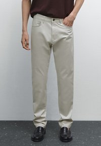 Beige chinos i bomullsblandning med rak benmodell, framfickor och knappstängning, i kombination med svarta loafers.