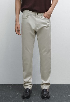 Beige chinos made of cotton blend, featuring a straight leg design, front pockets, and a button closure, paired with black loafers.