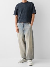 Mörkblå kortärmad t-shirt i kombination med ljusblå vida jeans. Vita sneakers fulländar outfiten. Släta tygstrukturer synliga.