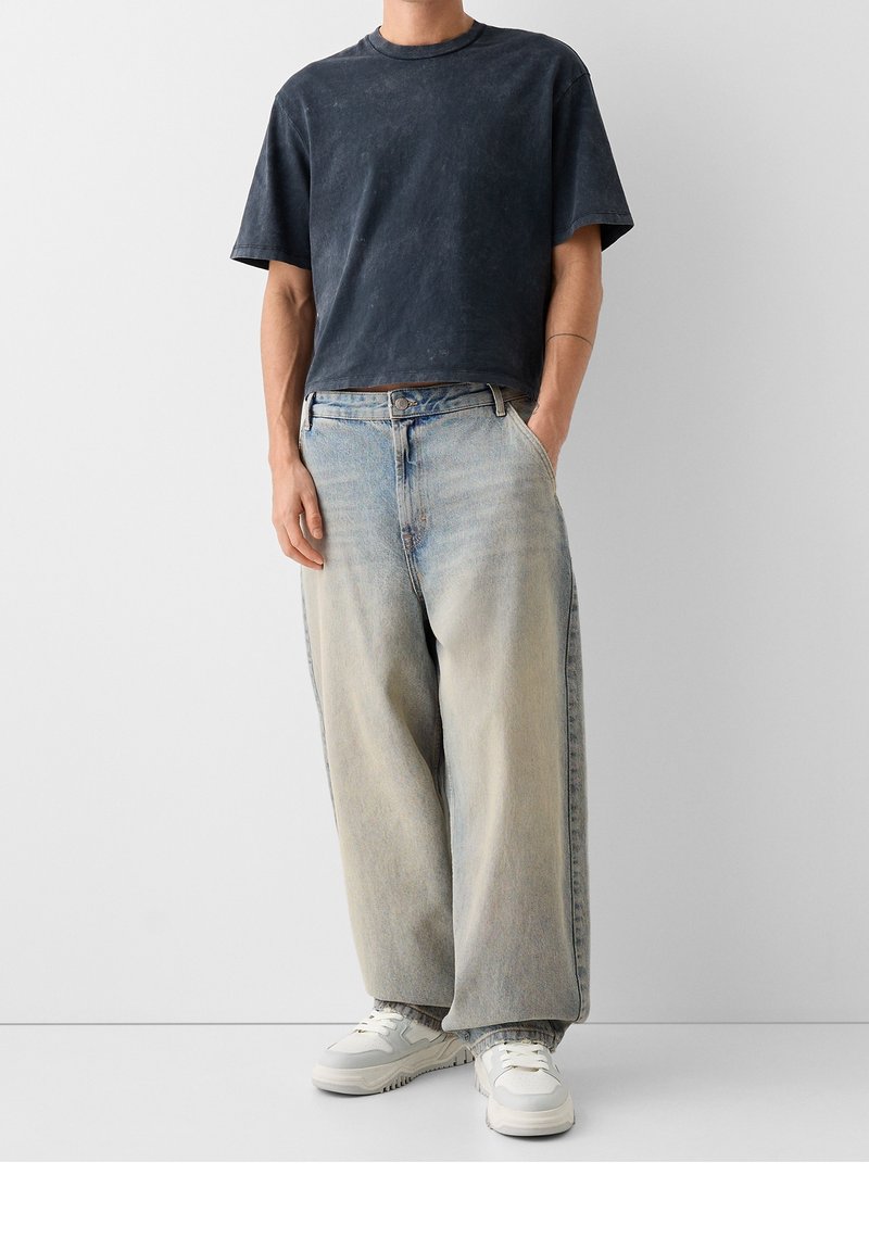 Mörkblå kortärmad t-shirt i kombination med ljusblå vida jeans. Vita sneakers fulländar outfiten. Släta tygstrukturer synliga.