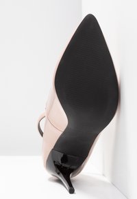 Chaussure à talons hauts en cuir verni rose, à bout pointu et semelle en caoutchouc noir, avec un talon fin et une texture côtelée sous la semelle.
