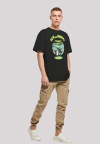 Fekete pamut póló, amelyen egy színes "Rick és Morty" grafika látható, khaki cargo nadrággal és fehér sportcipőkkel viselve.