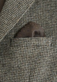Blazer din tweed în tonuri de gri și maro, cu un finisaj texturat. Un pătrat de buzunar maro cu model este vizibil în buzunarul din față.