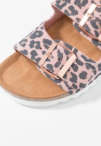 Różowe sandały w panterkę z dwoma regulowanymi paskami, różowozłotymi klamrami, korkową wkładką i białą teksturowaną podeszwą.