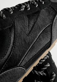 Le scarpe da ginnastica nere presentano materiali misti: una tomaia in pelle liscia con accenti in pelliccia testurizzata, lacci bianchi a contrasto e una suola di colore chiaro.