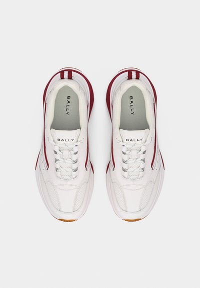 Λευκά και κόκκινα χαμηλά αθλητικά παπούτσια Bally με κορδόνια, επωνυμίες στην εσωτερική σόλα και λαστιχένιες σόλες, φωτογραφημένα από πάνω σε απλό φόντο.