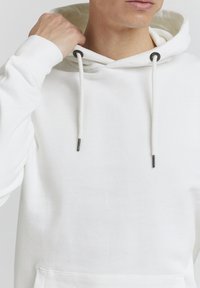 Witte hoodie met een trekkoordcapuchon, ribgebreide manchetten en onderkant. Bevat een gestructureerde stof, met metalen punten op de trekkoorden.