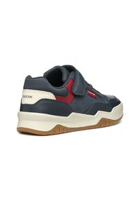 Zapatilla de deporte azul marino con parte superior de cuero y malla, correa de velcro, acento rojo contrastante, media suela blanca acolchada y suela de goma.