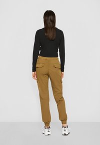 Pantalones cargo caqui con puños elásticos y múltiples bolsillos laterales, combinados con una camiseta negra ajustada de manga larga, vistos desde la espalda.