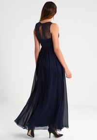 Marinblå maxiklänning med genomskinligt övre parti och nyckelhål bakdesign. Lätt, flödande tyg med full kjol. Bärs med svarta klackar.