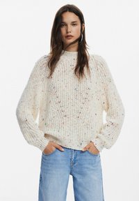 Maglione chunky cream con collo alto, polsini a coste e un motivo testurizzato, caratterizzato da macchie colorate sparse.