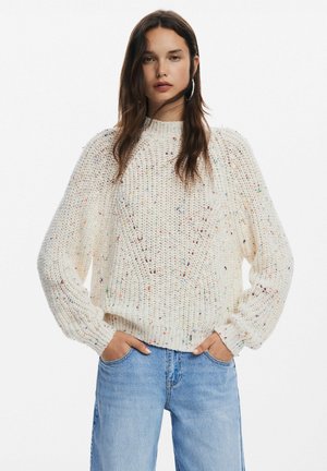 Maglione chunky cream con collo alto, polsini a coste e un motivo testurizzato, caratterizzato da macchie colorate sparse.