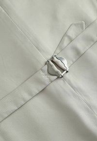 Helles graues Gewebe mit glatter Textur, ausgestattet mit einem silbernen Metallverschluss und einem spitzen Taschenklappen-Detail. Sauberes, minimalistisches Design.
