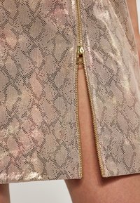 Gonna in ecopelle rosa metallica con una stampa a serpente, dotata di una zip laterale dorata e una superficie testurizzata per un tocco di dettaglio in più.